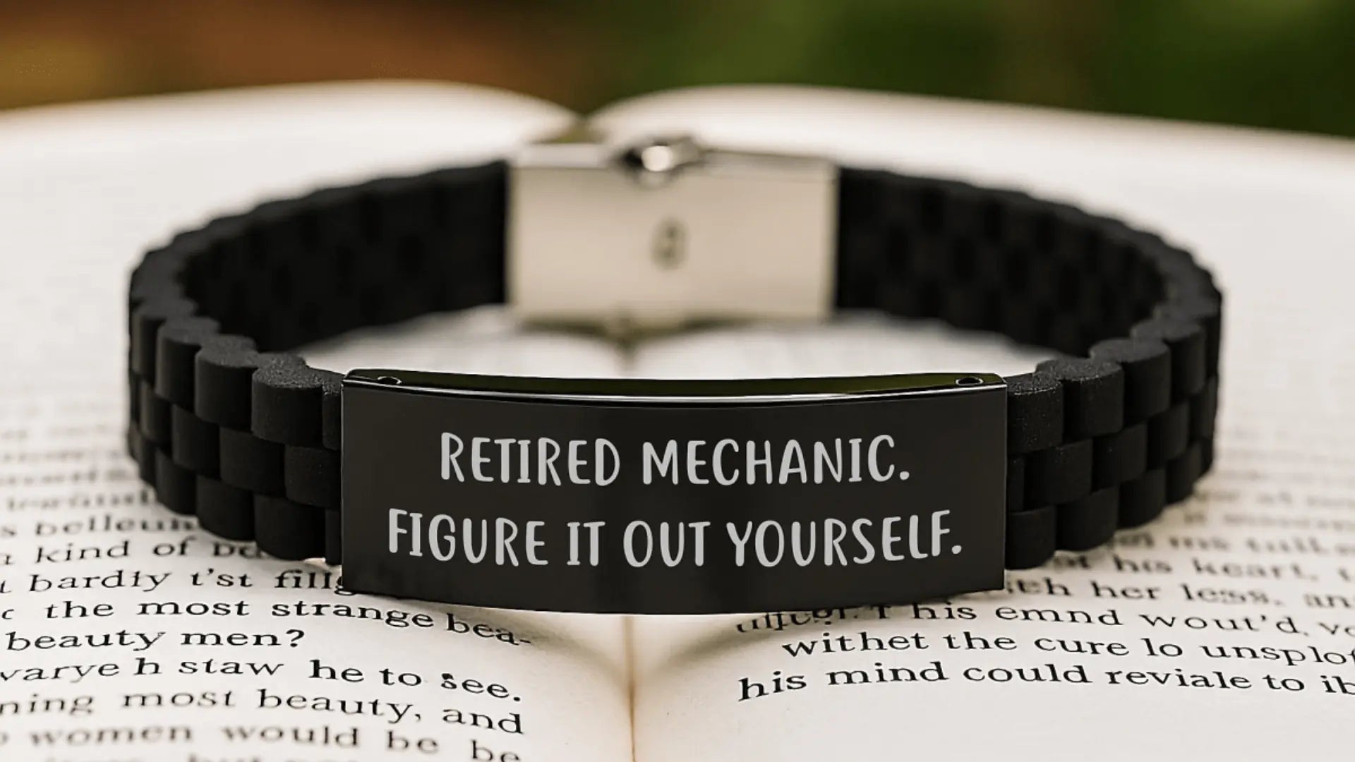 Black engraved bracelet reading retired mechanic resting on an open book