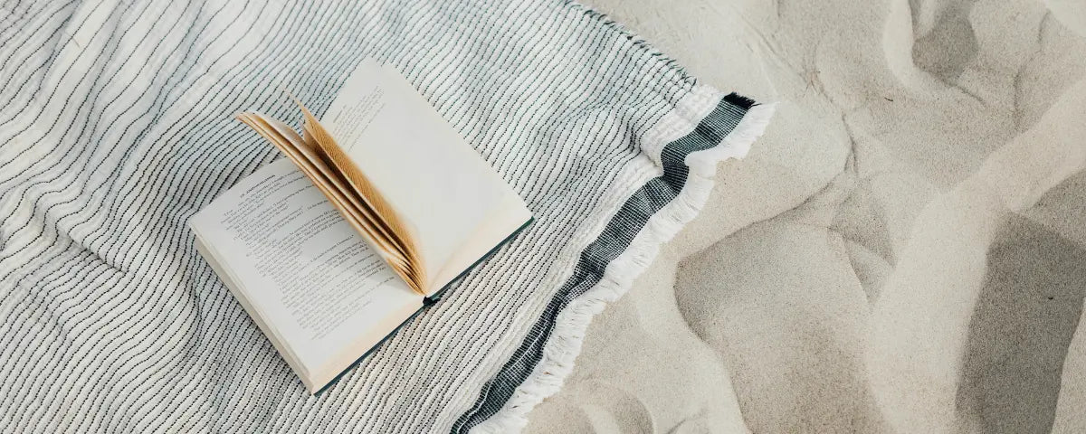 folded cream beach towel and a gold pen resting on pale sand, a personalized gift idea for dad