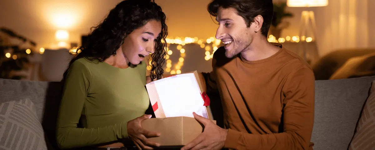 Young woman opening a custom gift from her husband under warm string lights