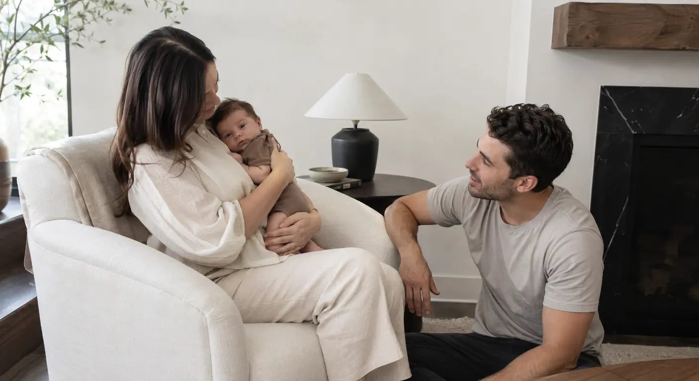 Mother holding her baby in an armchair while dad sits nearby on their first mother's day