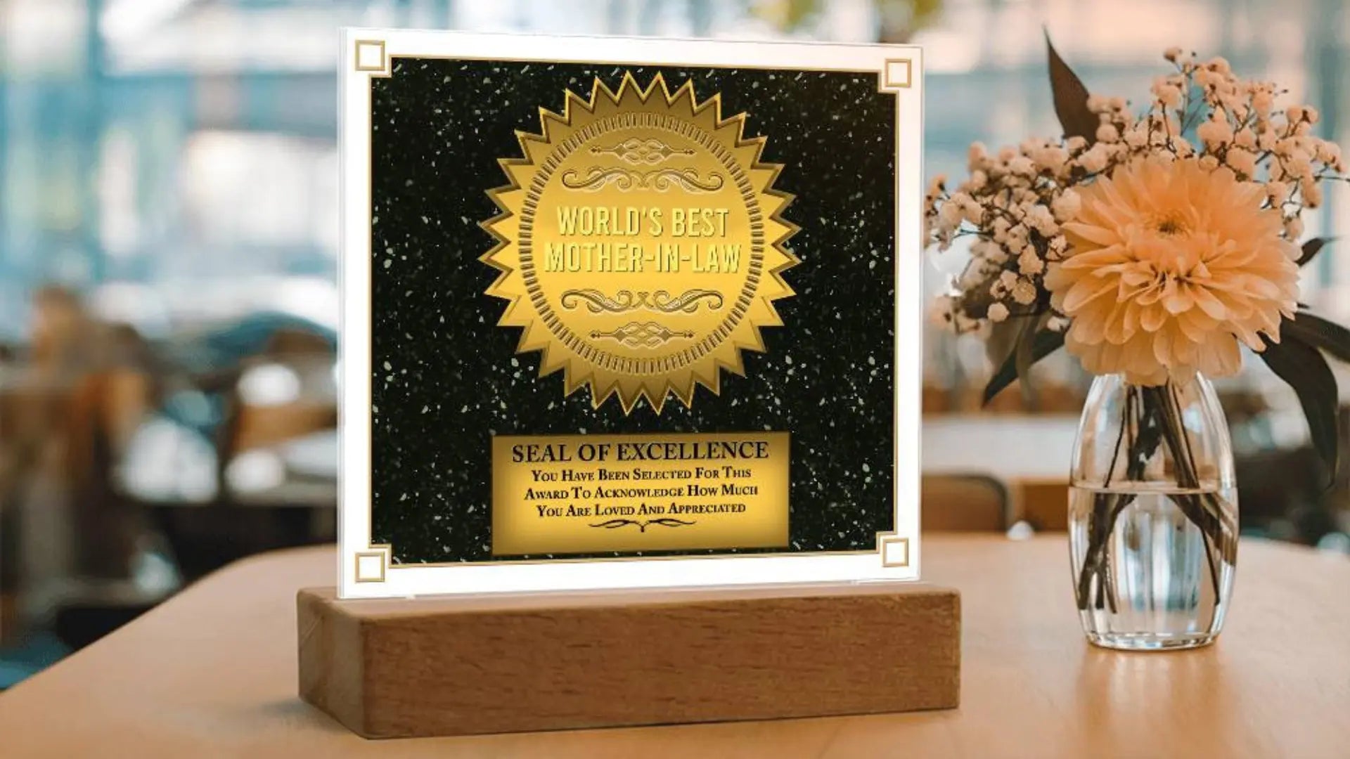 Engraved black and gold plaque on a wooden stand beside flowers, a mother in law gift
