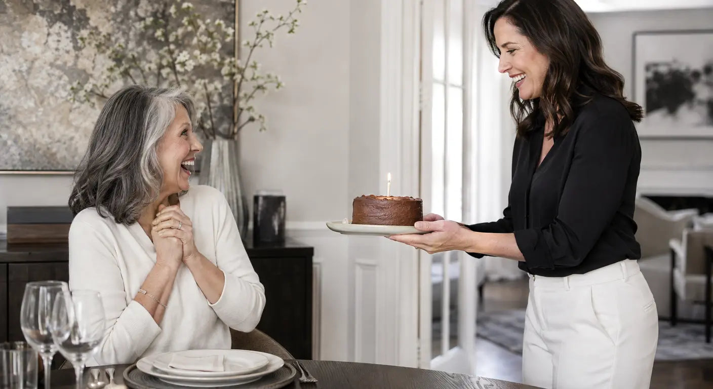 Young woman carrying a chocolate birthday cake to her smiling mother at a set table