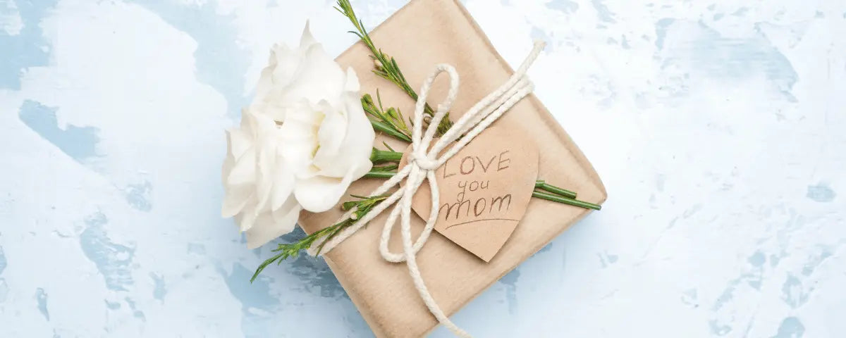 Kraft paper gift box tied with ribbon and a white rose on pale blue, a thoughtful gift for mom
