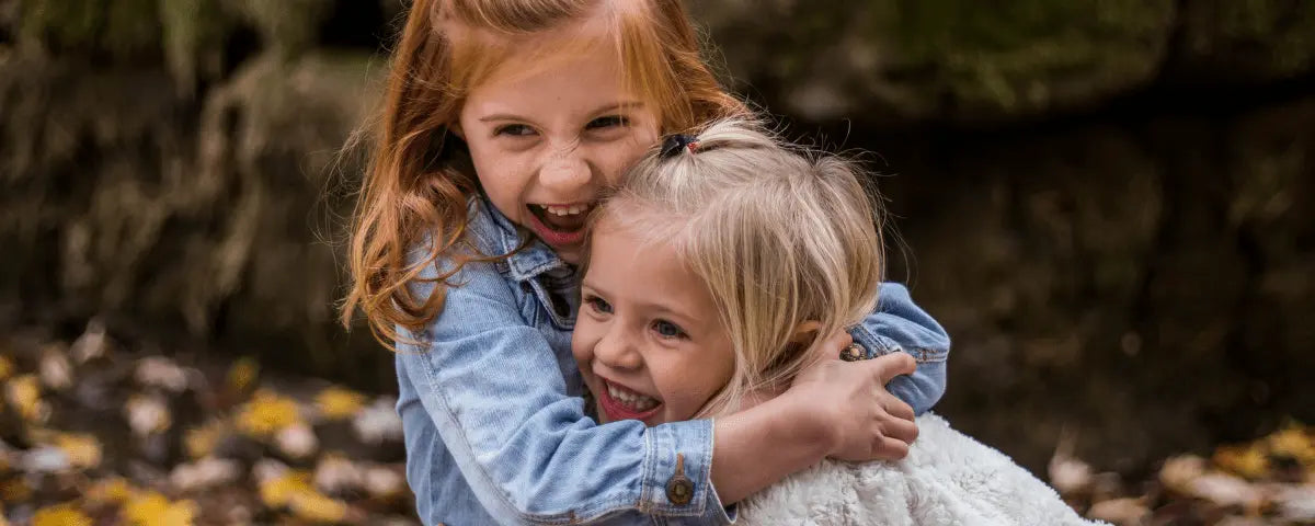 Two little girls hugging and laughing outdoors, unbiological sisters by choice